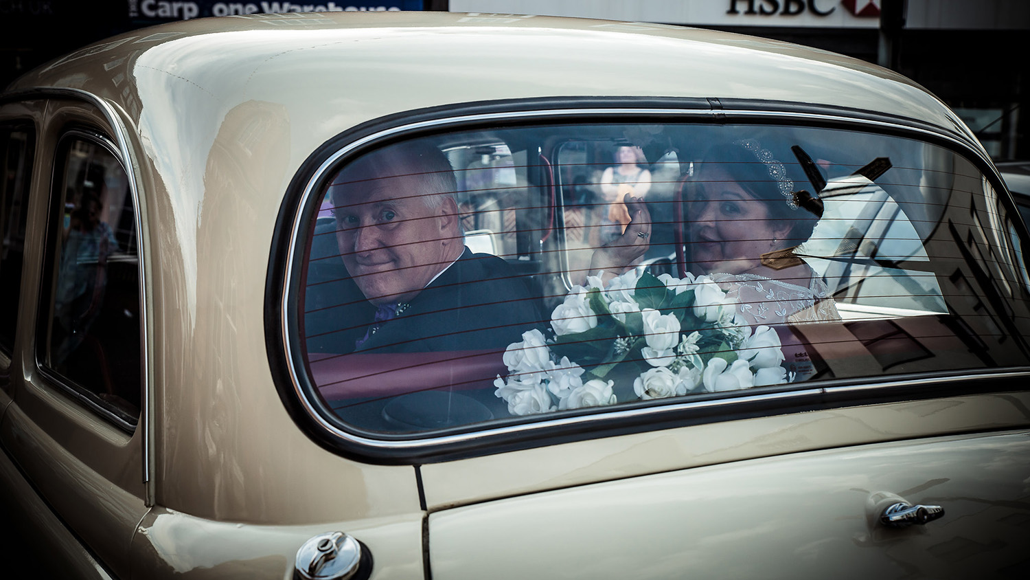 Rear window view of passengers seated inside a classic taxi cab, burgundy leather interior visible with natural light entering the cabin.