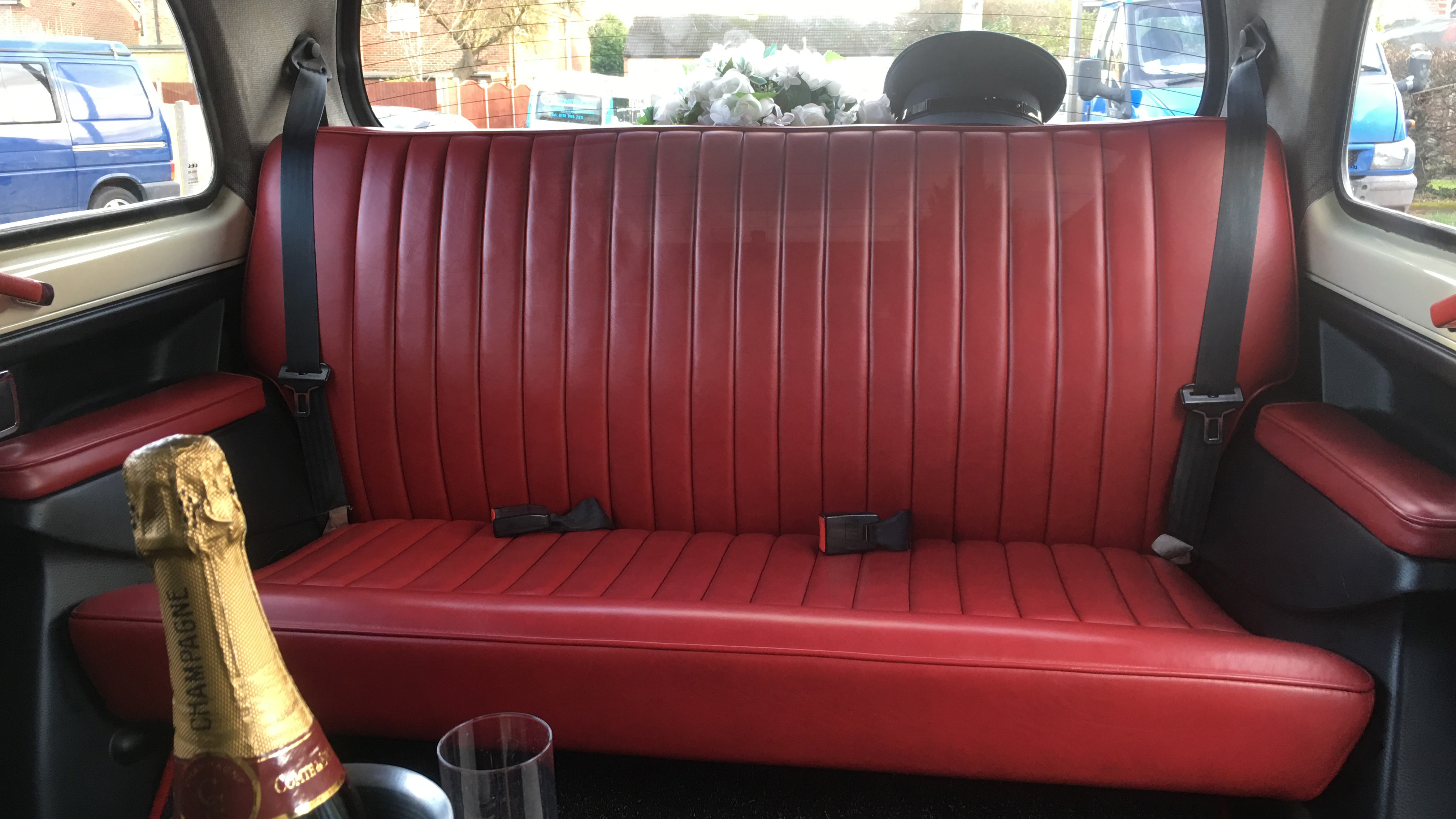 Rear bench seating inside a classic taxi cab with burgundy leather upholstery and spacious cabin layout.