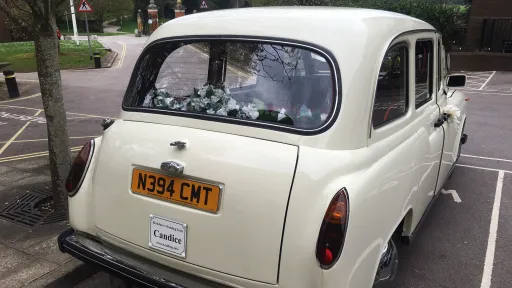 Rear view of a classic taxi cab showing parcel shelf with decorations and registration plate, parked in a car park.