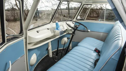Front interior of a VW split screen campervan with turquoise bench seating, steering wheel and dashboard in classic vintage style.