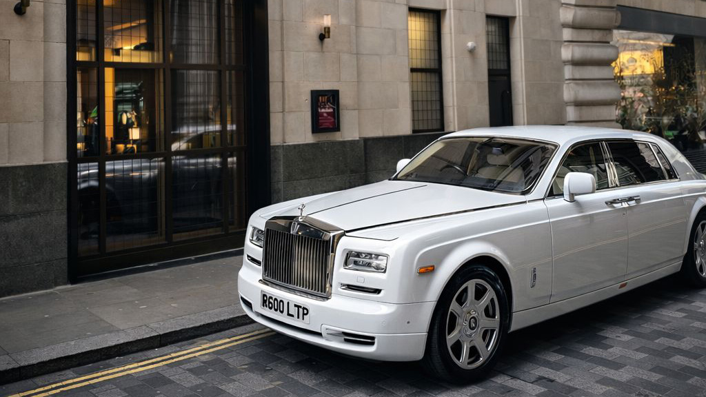 White Rolls-Royce Phantom parked outside a building entrance in a city setting, side profile showing long wheelbase design.