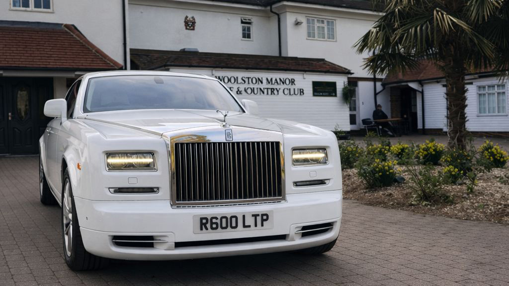 Front view of a white Rolls-Royce Phantom with large chrome grille and Spirit of Ecstasy, parked on a driveway.