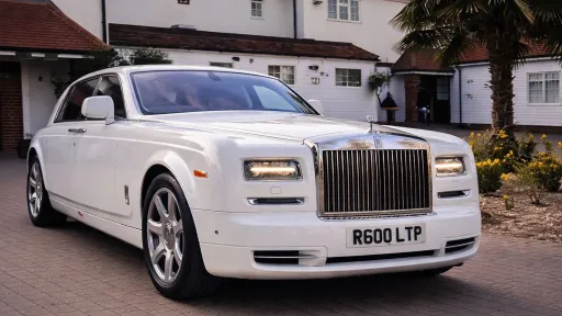 White Rolls-Royce Phantom parked outside a wedding venue, angled view with palm trees and building in the background.