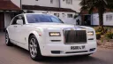 White Rolls-Royce Phantom parked outside a wedding venue, angled view with palm trees and building in the background.