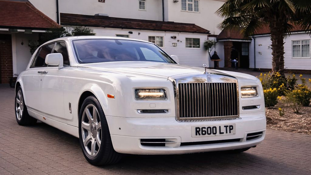White Rolls-Royce Phantom parked outside a wedding venue, angled view with palm trees and building in the background.