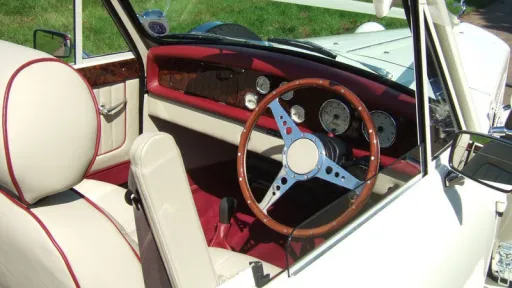 Driver’s area of Beauford convertible with vintage steering wheel, cream dashboard and red trim, roof open allowing natural light into cabin.