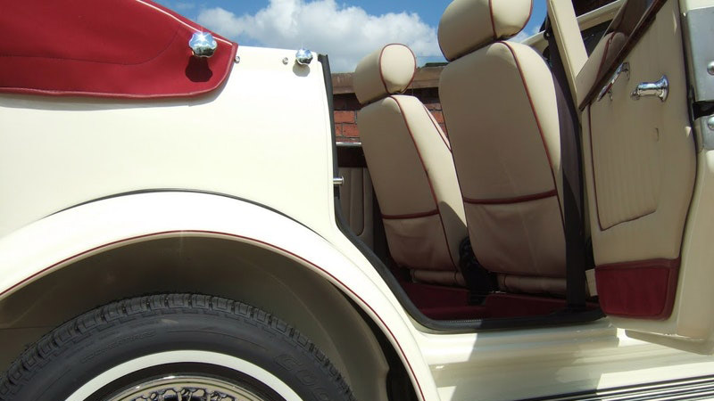 Rear passenger entry of cream Beauford convertible showing cream leather seats, red carpet and step access, door open with exterior wheel visible.
