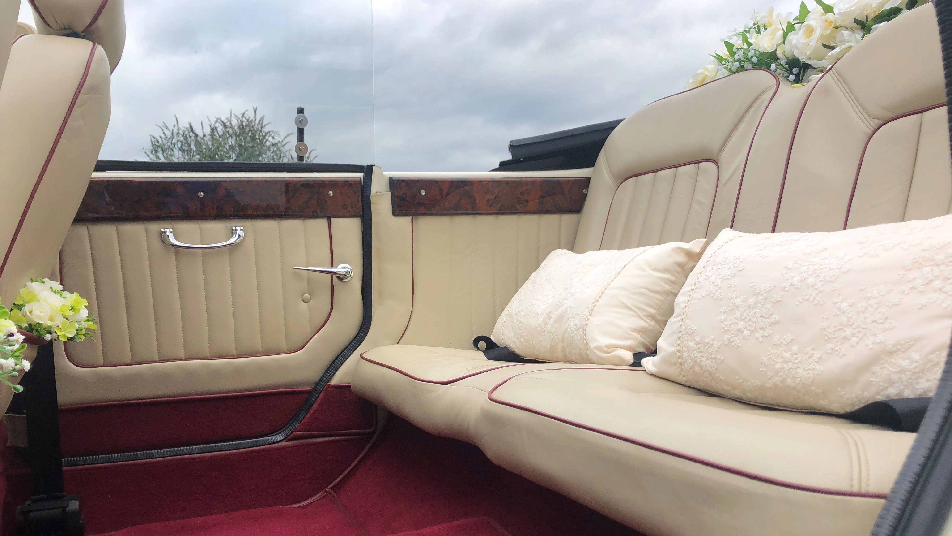 Close-up of rear seating in Beauford wedding car with cream leather upholstery and red carpet flooring, viewed from side door opening.