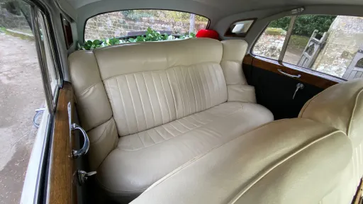 Interior of Rolls-Royce Silver Cloud showing cream leather rear seats, polished wood trim and spacious cabin with natural light.