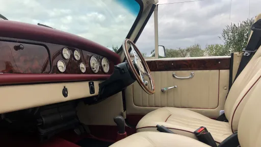 Interior of Beauford convertible showing cream leather seats, red carpeting and classic dashboard, door open highlighting spacious rear seating area.