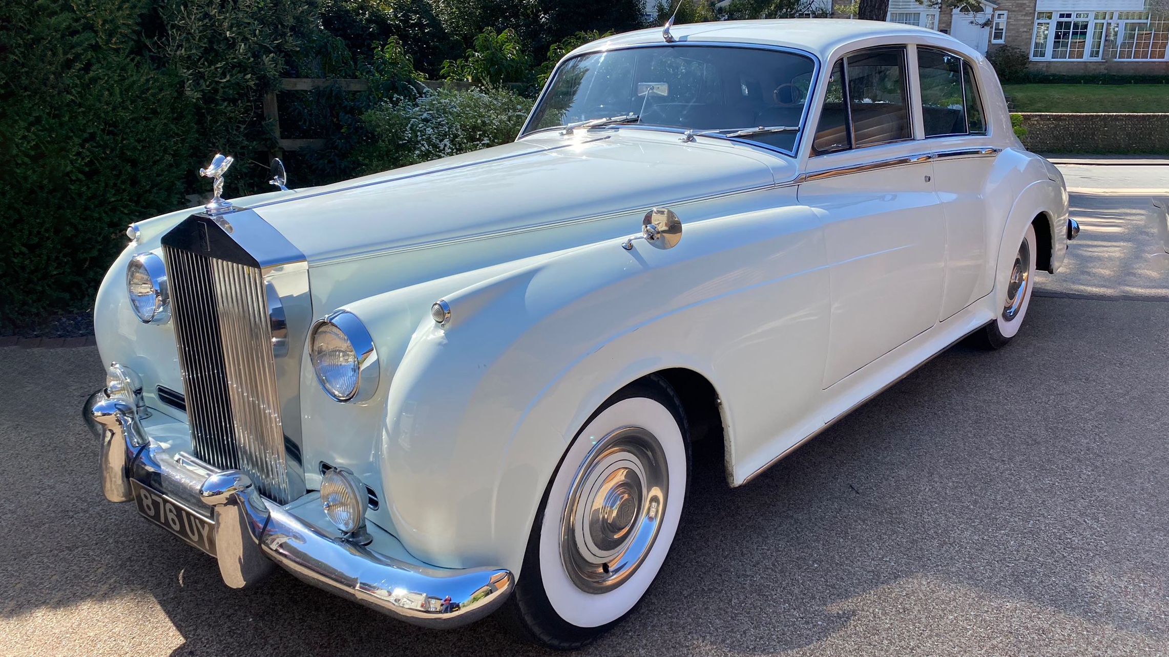 Front three-quarter view of 1957 Rolls-Royce Silver Cloud in Old English White parked on driveway, sunlight reflecting on chrome