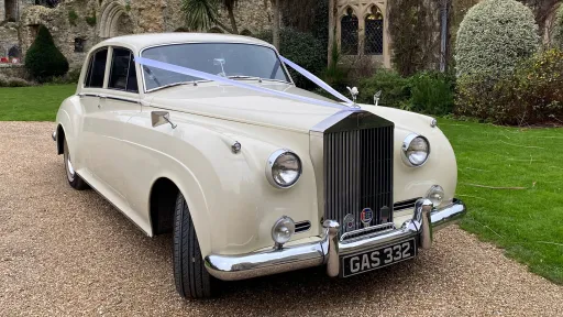 Front right view of Rolls-Royce Silver Cloud in Old English White decorated with wedding ribbons, parked on gravel drive.