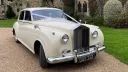 Front right view of Rolls-Royce Silver Cloud in Old English White decorated with wedding ribbons, parked on gravel drive.