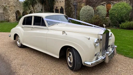 Side angle of Rolls-Royce Silver Cloud in Old English White parked on driveway, showing long body shape and classic styling.