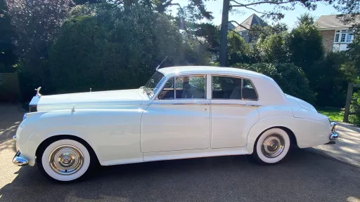 Full left side profile of 1957 Rolls-Royce Silver Cloud in Old English White with whitewall tyres, parked on driveway