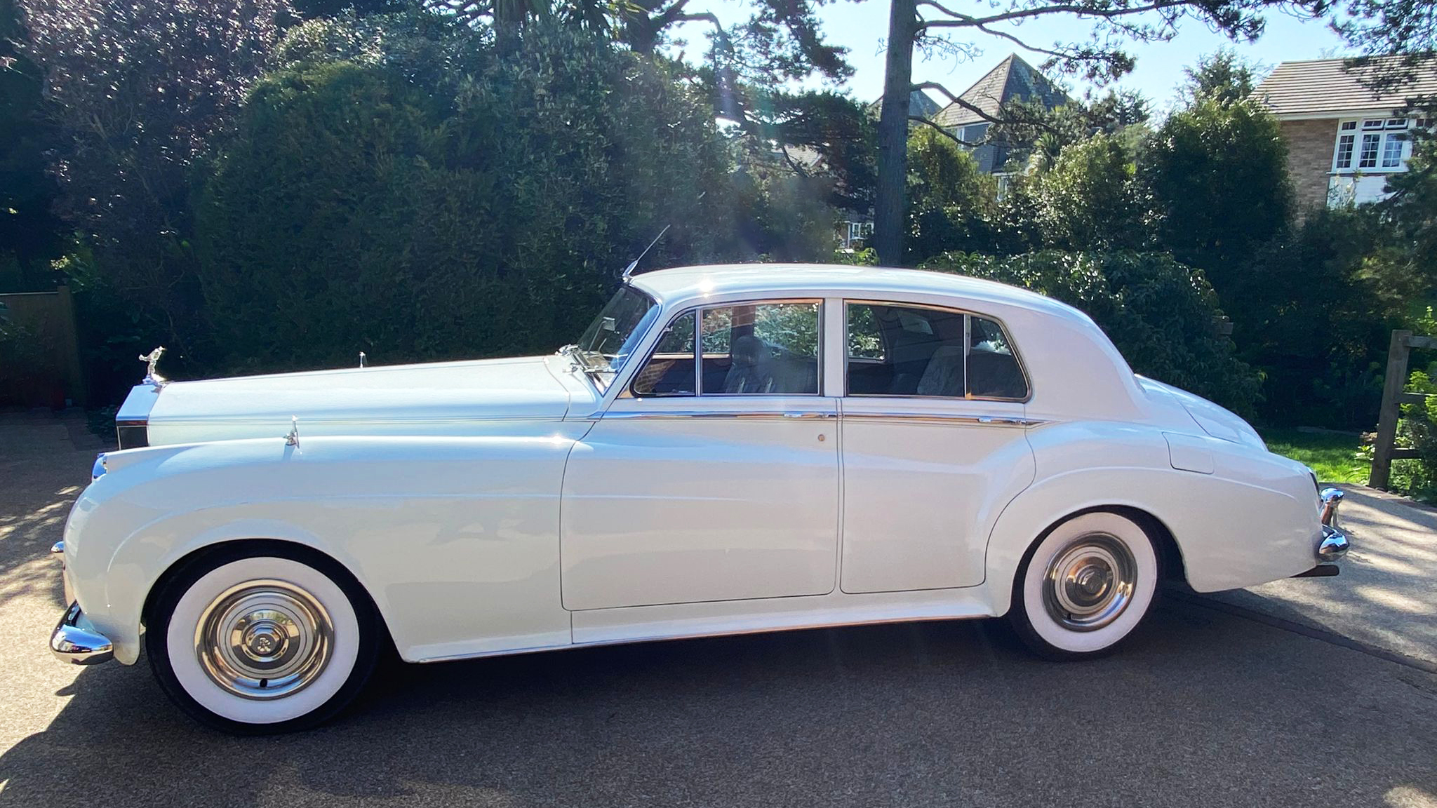 Full left side profile of 1957 Rolls-Royce Silver Cloud in Old English White with whitewall tyres, parked on driveway
