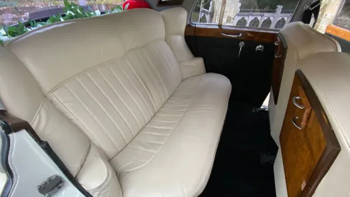 Rear bench seat of Rolls-Royce Silver Cloud with cream leather upholstery, wood trim and spacious legroom.