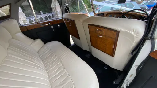 Interior view of Rolls-Royce Silver Cloud showing cream leather seating, door wood panels and classic luxury finish.