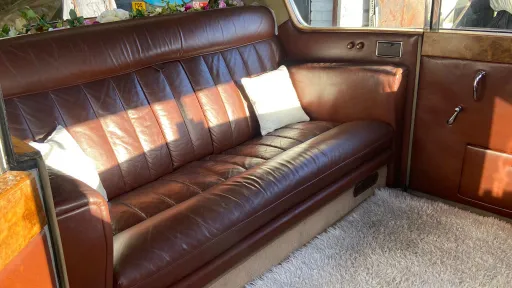 Wide view of Austin Princess limousine rear interior with brown leather bench seat, occasional seats folded away highlighting generous legroom and cabin space