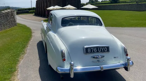 Rear view of Rolls-Royce Silver Cloud in Old English White showing curved boot design and chrome bumper, outdoor setting
