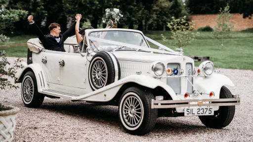 Bride and groom seated inside cream Beauford convertible with roof open and chauffeur driving, showing spacious rear seating.