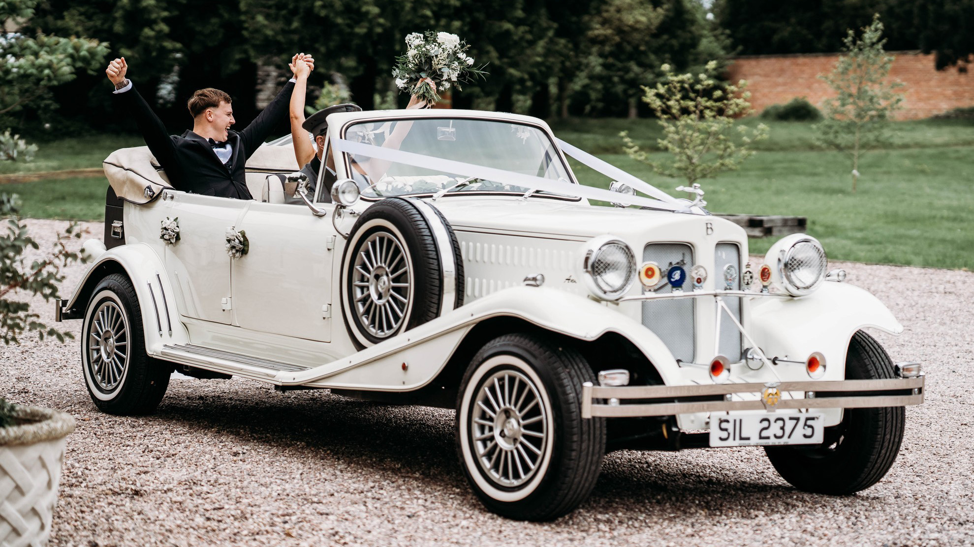 Bride and groom seated inside cream Beauford convertible with roof open and chauffeur driving, showing spacious rear seating.