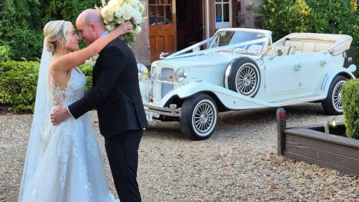 bride-and-groom-kissing-in-front-of-a-convertible-vintage-car.jpg
Bride and groom kissing beside cream Beauford wedding car with convertible roof down, parked on gravel driveway.