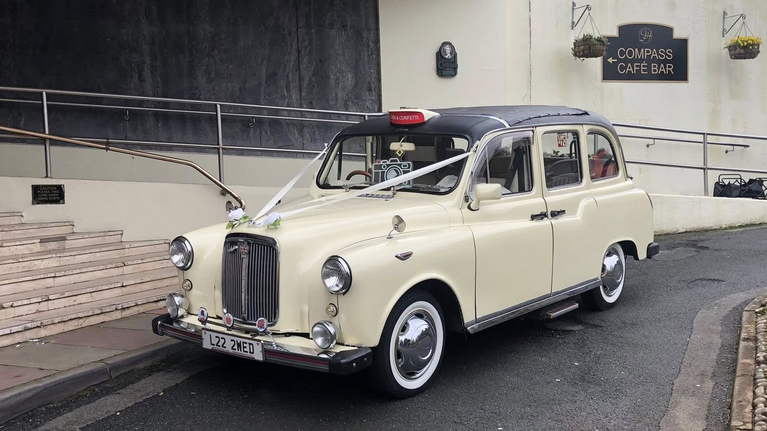 Classic taxi cab in ivory with chrome details and white wall tyres, parked outside a venue in Devon.