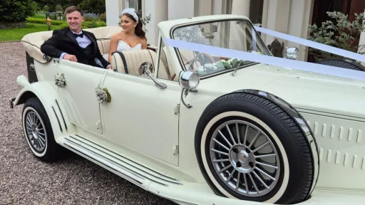 Couple smiling inside cream Beauford convertible with roof down, showing open top and classic interior.
