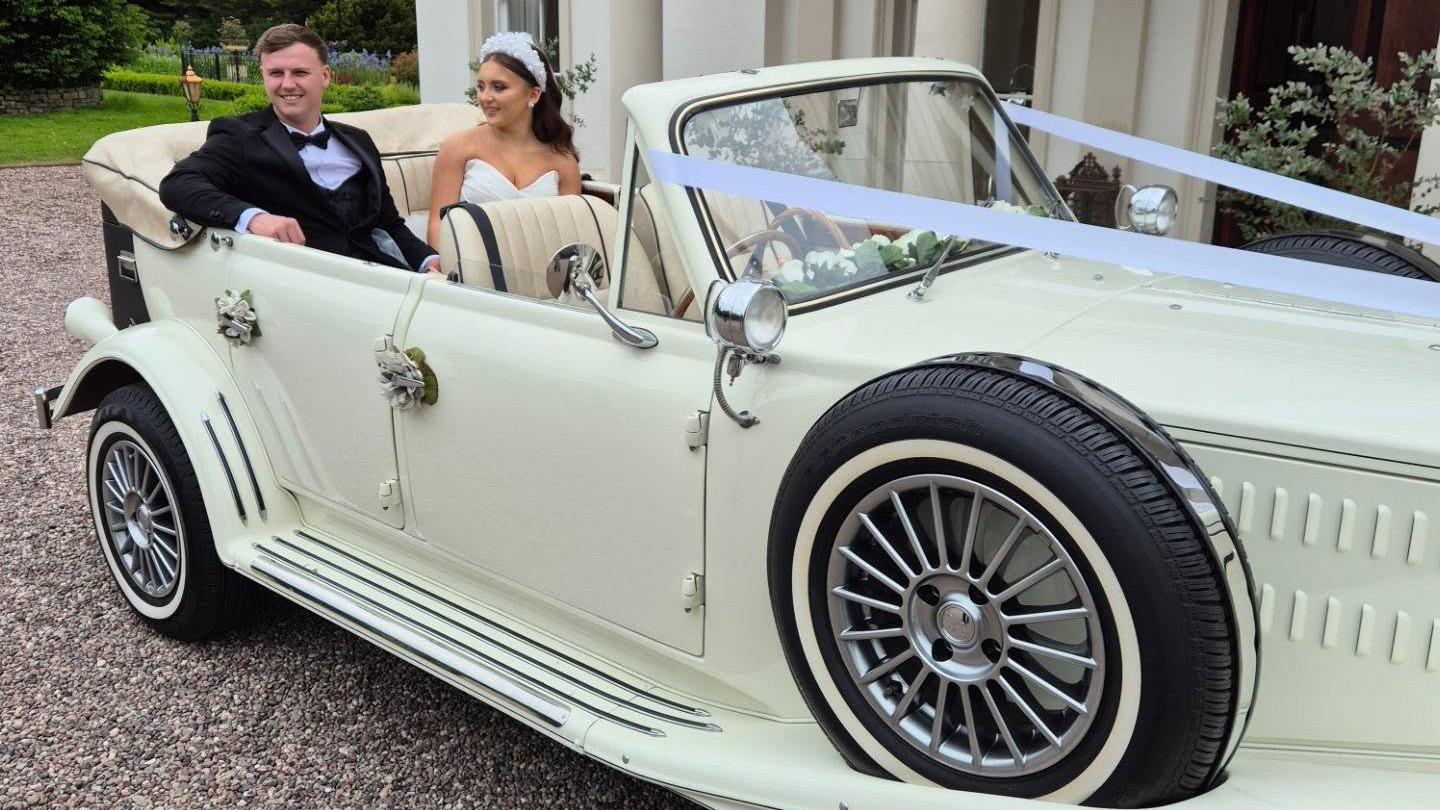 Couple smiling inside cream Beauford convertible with roof down, showing open top and classic interior.