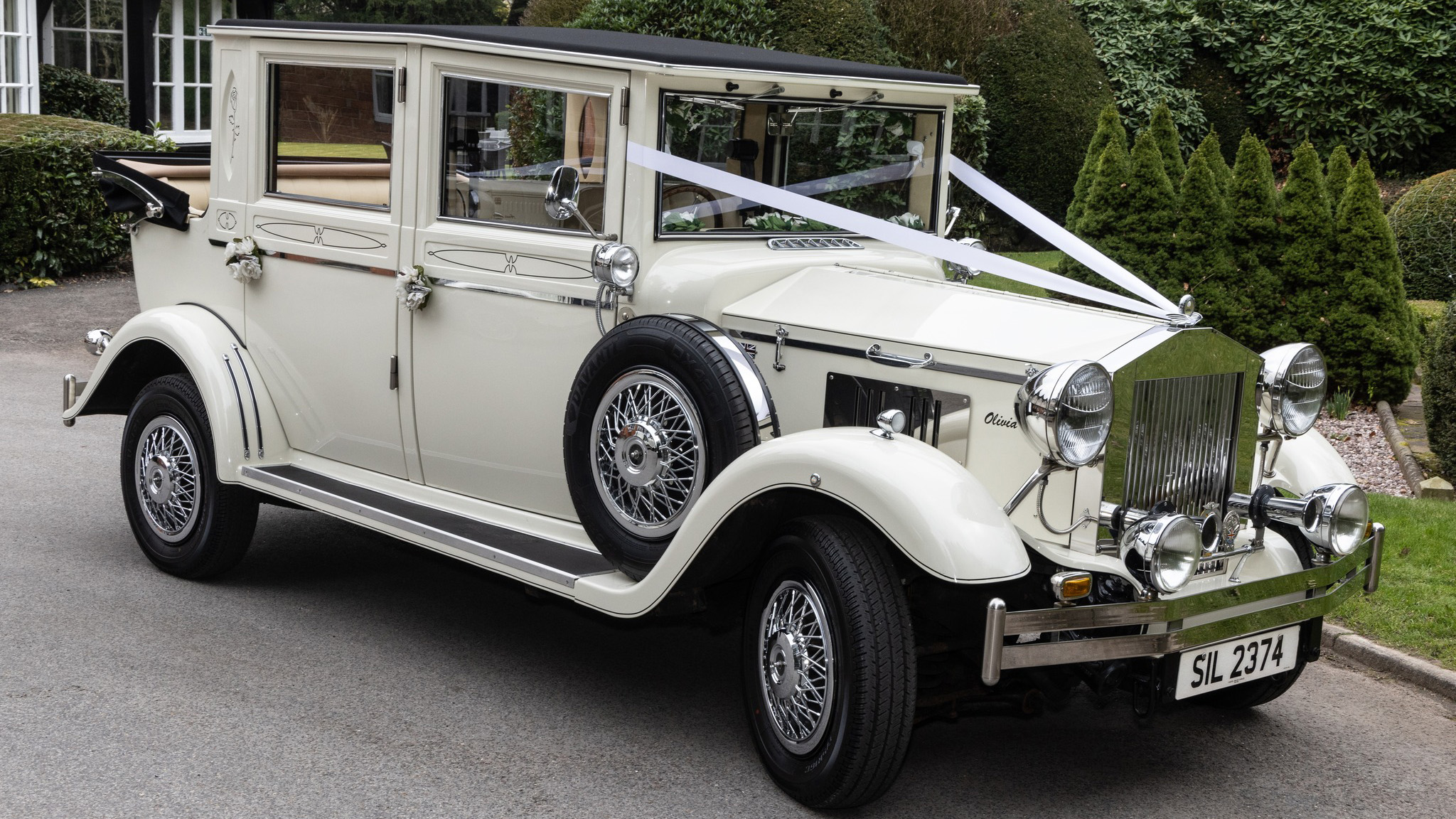 Cream 1930s style Imperial wedding car with chrome headlights and side-mounted spare wheel, parked on a driveway in Cheshire.