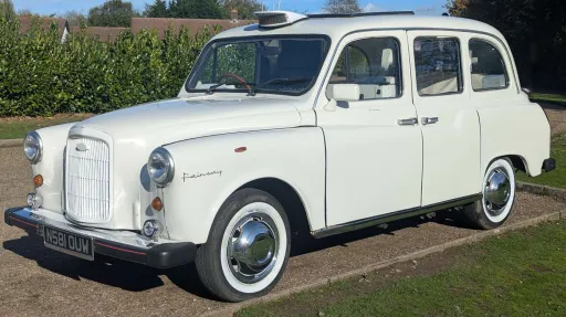 Front left view of classic Fairway taxi cab in Old English White with white wall tyres, parked on a driveway.