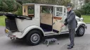Uniformed chauffeur opening rear door of cream Imperial wedding car with black soft top roof and chrome detailing.
