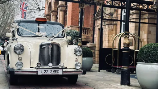 Ivory classic taxi cab with wedding ribbons parked in Paignton, Devon, front three-quarter view.