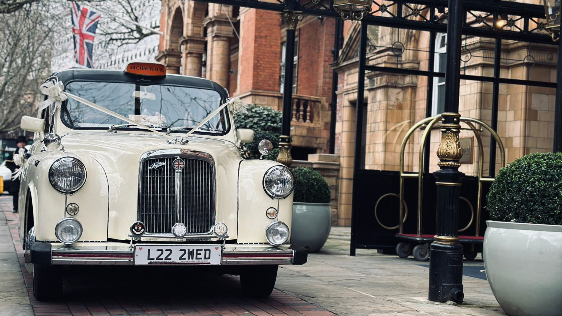 Ivory classic taxi cab with wedding ribbons parked in Paignton, Devon, front three-quarter view.