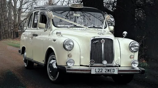 Vintage London-style taxi cab in ivory with chrome grille and round headlights, parked on a road.