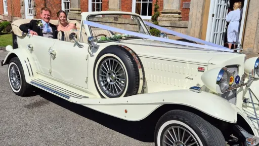 Newlywed couple seated inside open top Beauford convertible decorated with wedding ribbons.