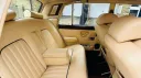 Rear bench seat of Rolls-Royce Silver Shadow Mk2 in cream leather with armrest and detailed stitching, showing luxury finish.