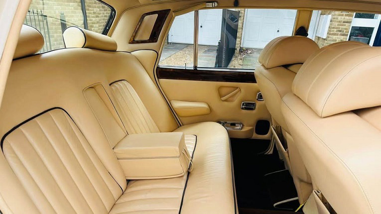 Rear bench seat of Rolls-Royce Silver Shadow Mk2 in cream leather with armrest and detailed stitching, showing luxury finish.