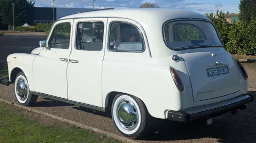 Rear left angle of classic Fairway taxi cab in Old English White, highlighting curved body and chrome details.