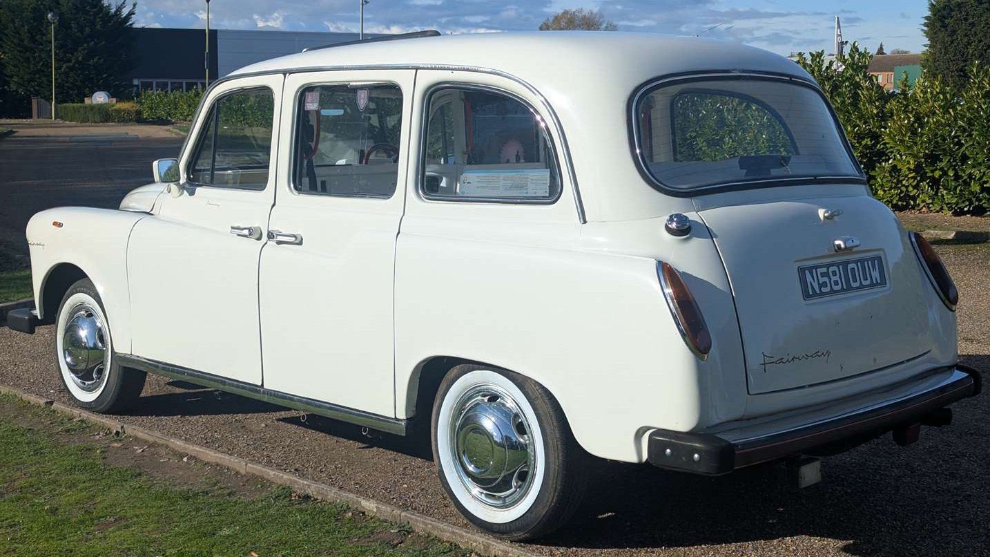 Rear left angle of classic Fairway taxi cab in Old English White, highlighting curved body and chrome details.