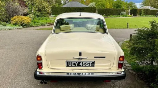 Rear view of Rolls-Royce Silver Shadow Mk2 in Old English White, showing chrome bumper and number plate, parked near landscaped gardens.