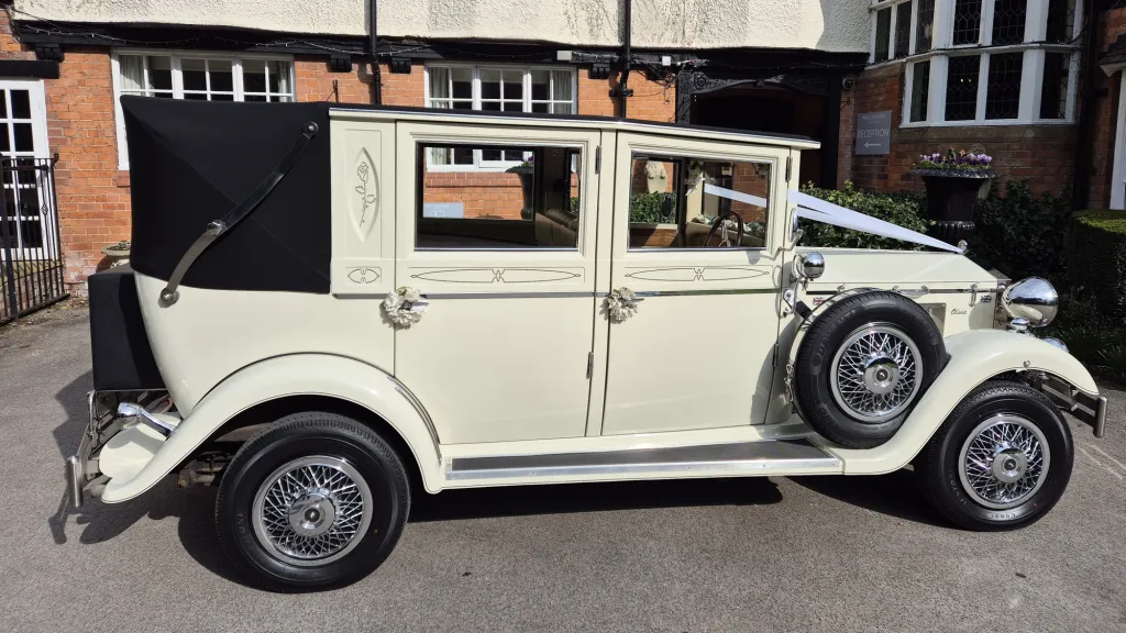 Full side view of cream Imperial wedding car with black soft top roof closed, chrome wheels and side-mounted spare.