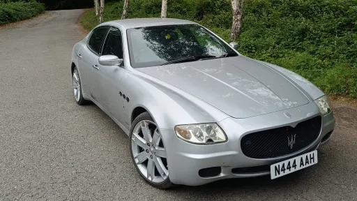 Silver Maserati Quattroporte parked on a quiet road, front three-quarter view highlighting sleek sporty design and alloy wheels.