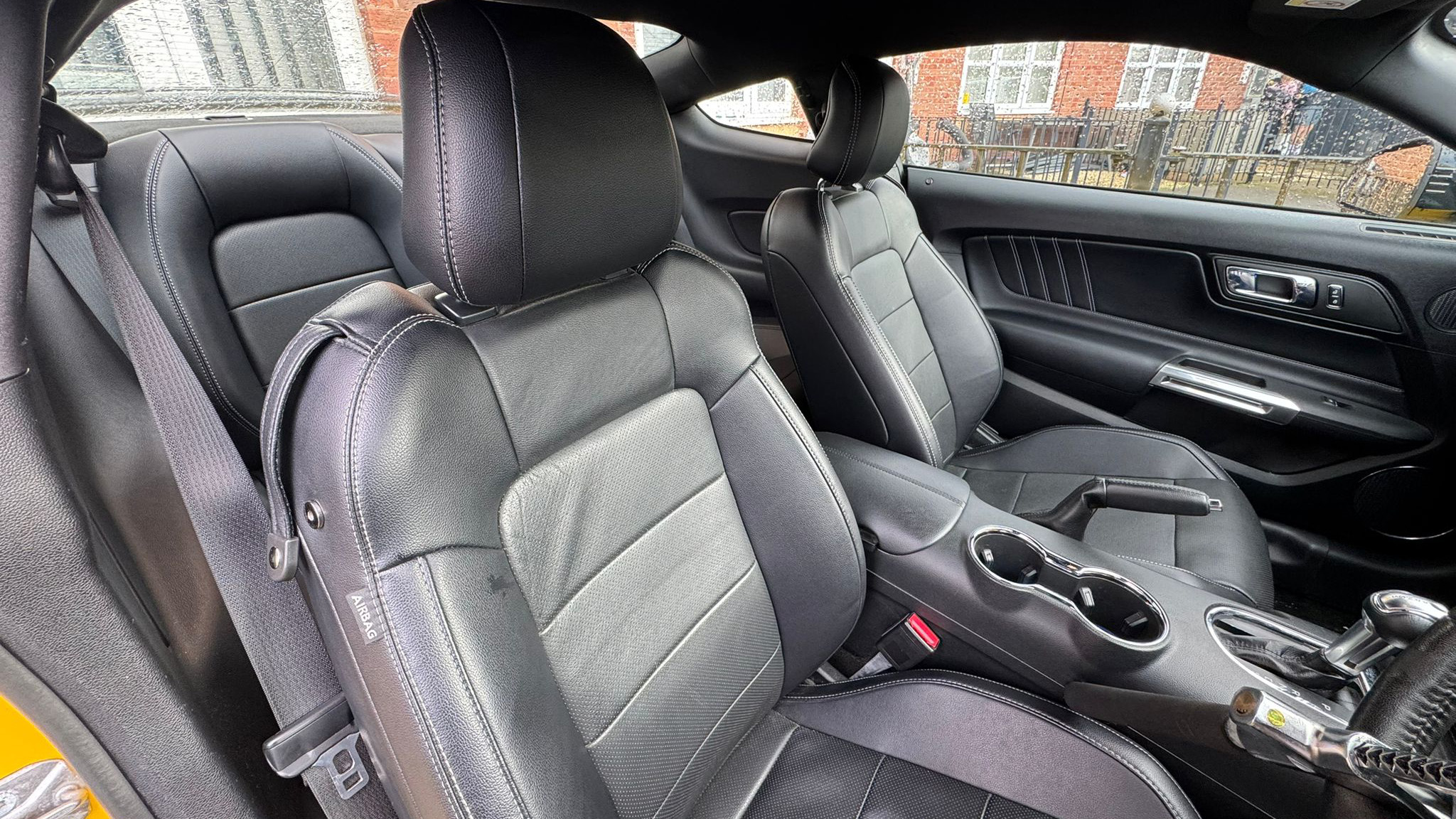 Front interior of Ford Mustang GT showing black leather seats, centre console and dashboard, sporty cabin with manual gear selector.