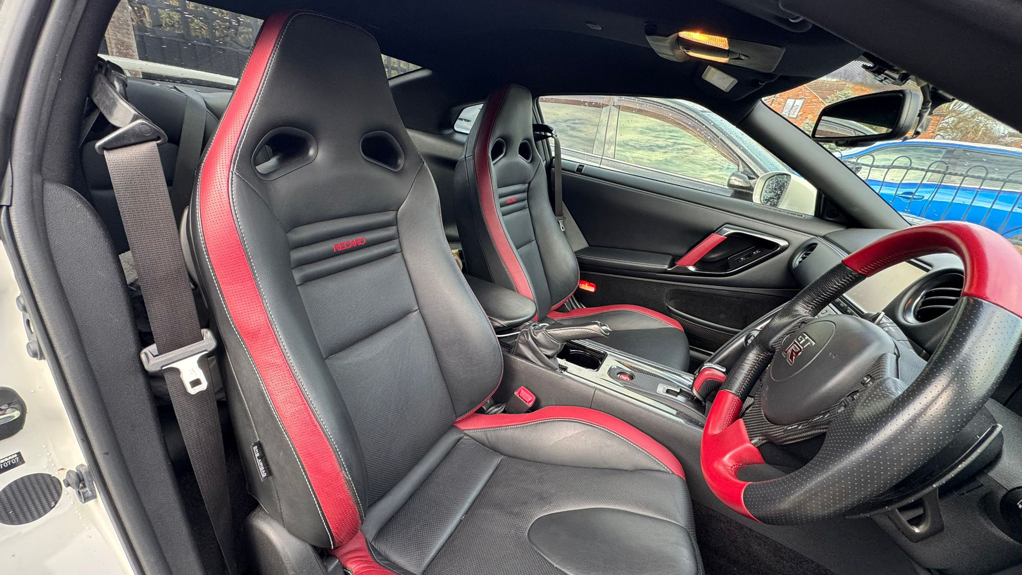 Front interior of white Nissan GTR R35 showing sporty bucket seats with red accents, steering wheel and centre console, performance-focused cabin.