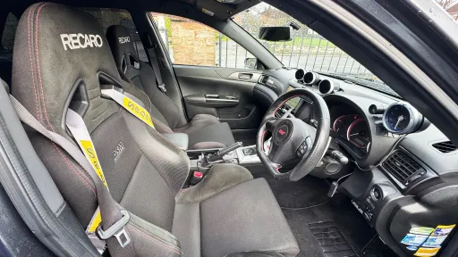 Front interior of Subaru Impreza showing sporty bucket seats, steering wheel and dashboard, dark upholstery with performance styling details.