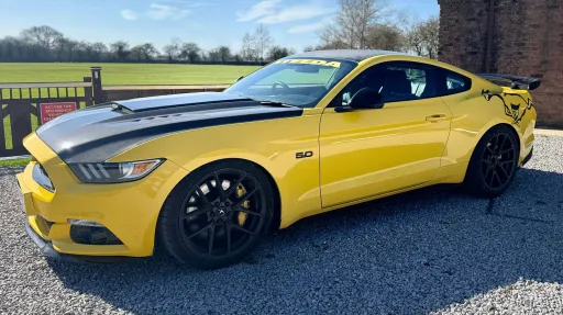 Yellow Ford Mustang GT wedding car with black roof and alloy wheels, angled view showing sporty coupe design in outdoor setting.