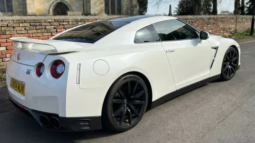 Rear three-quarter view of white Nissan GTR R35 with signature round tail lights and black wheels, parked on quiet residential street.