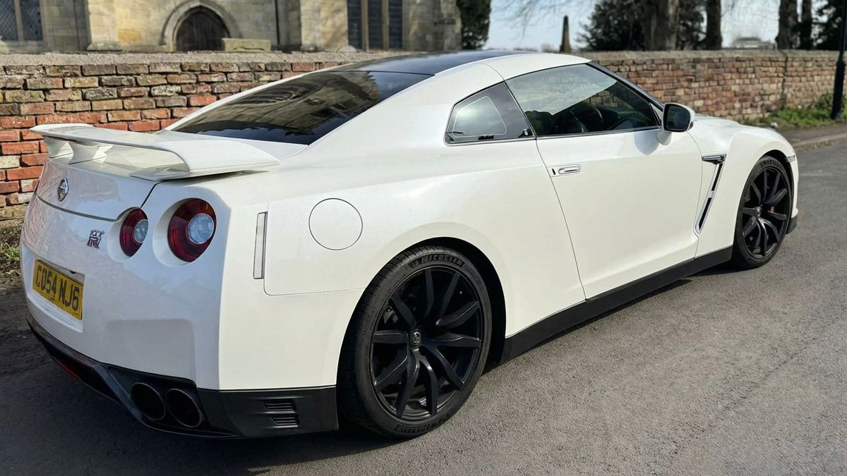 Rear three-quarter view of white Nissan GTR R35 with signature round tail lights and black wheels, parked on quiet residential street.